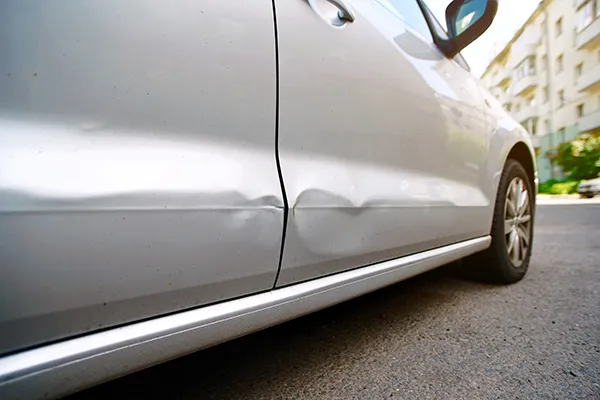 Long horizontal crease dent across the lower panels of a silver car door requiring professional paintless dent repair services.